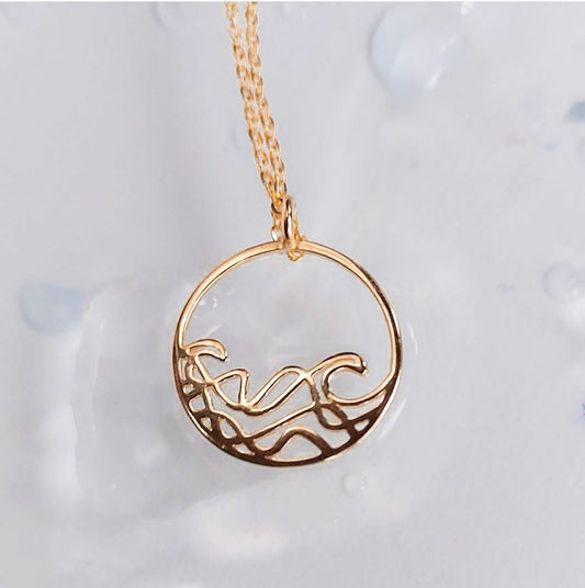 18k gold plated Petite Sombrio Ocean Surf Circle Necklace on a blur background, wave necklace, surf necklace
