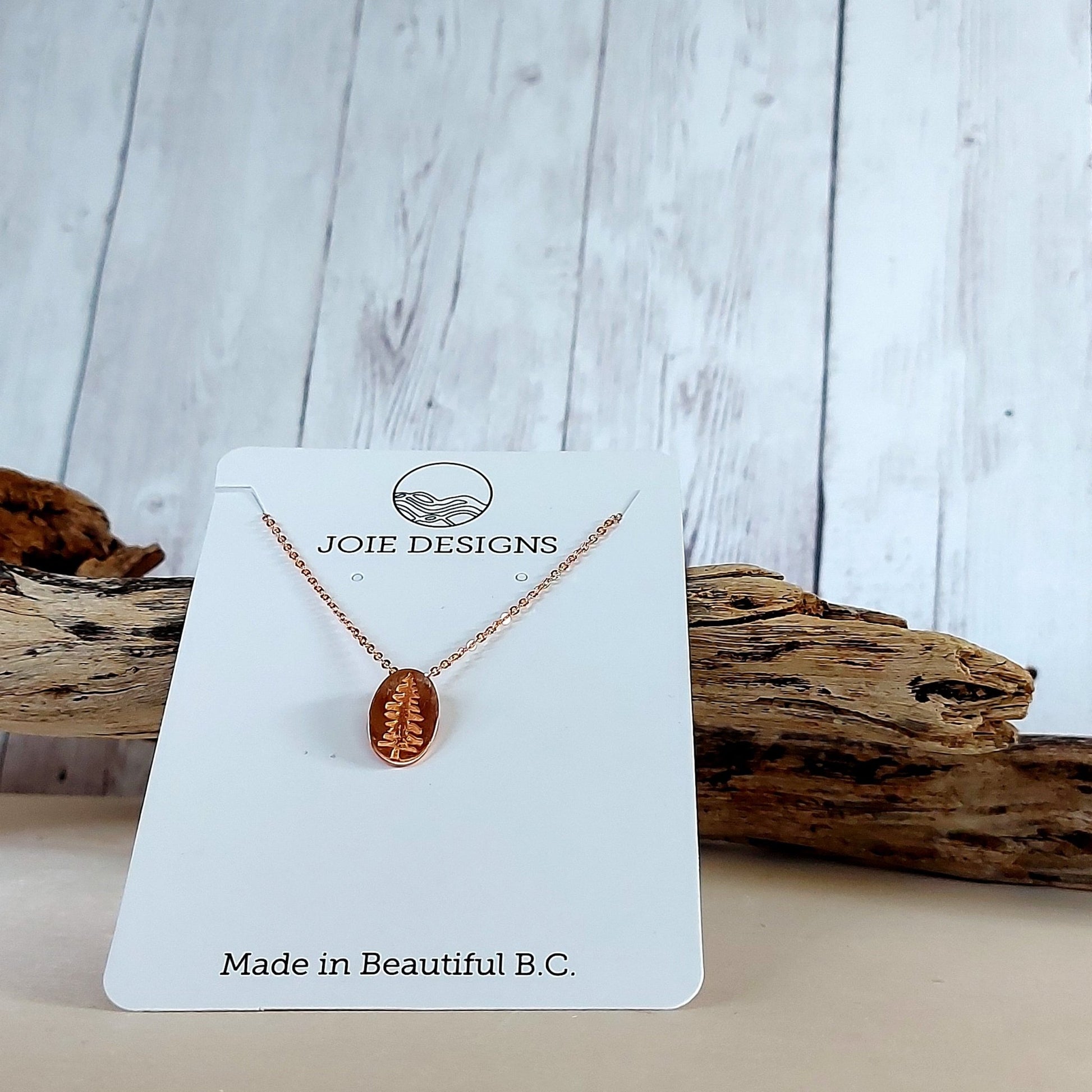 18k rose gold plated Sitka Tree Oval Dangle showcased on a jewelry card with wooden piece in background