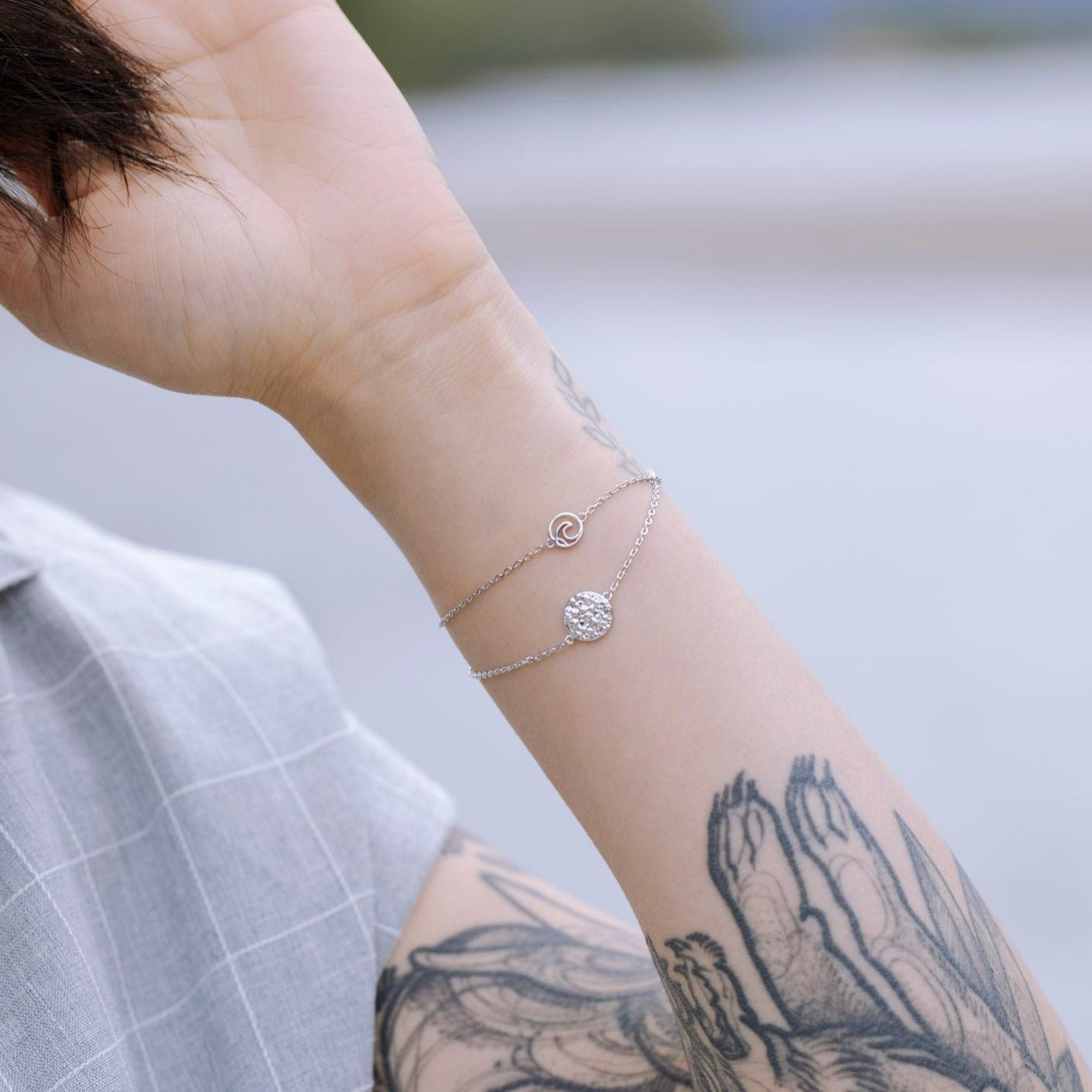 model wearing sterling silver Sol adjustable textured circle charm bracelet with nature water background