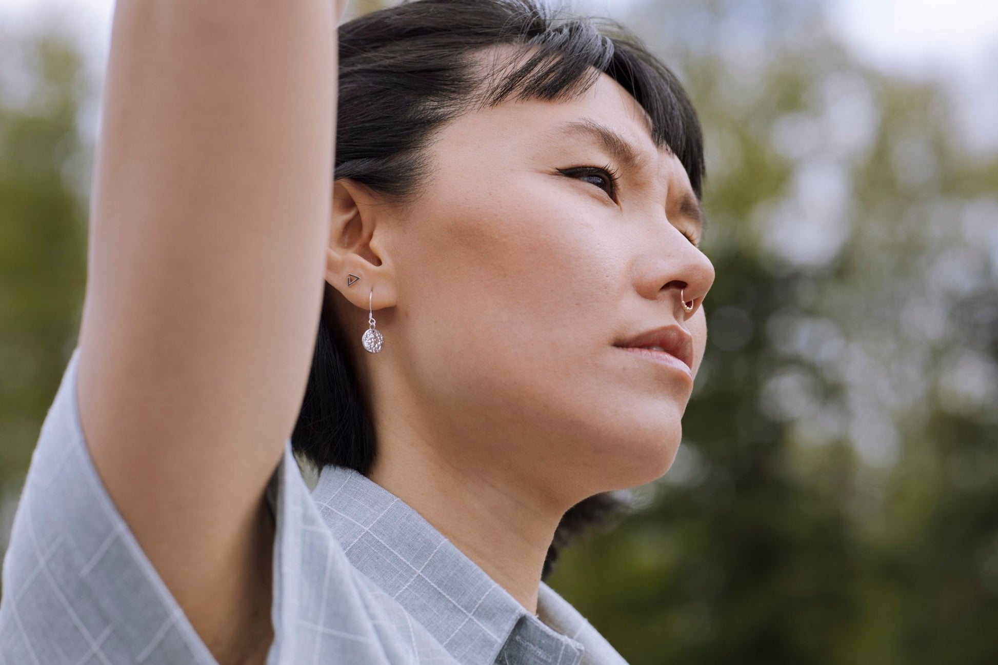 model wearing sterling silver Sol textured circle drop earrings with nature blur background - 2