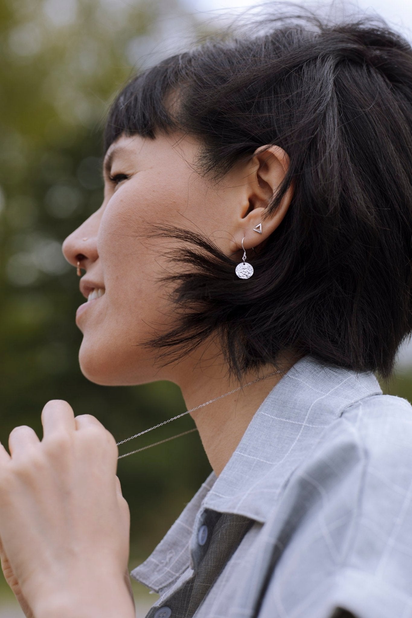 model wearing sterling silver Sol textured circle drop earrings with nature blur background - 1