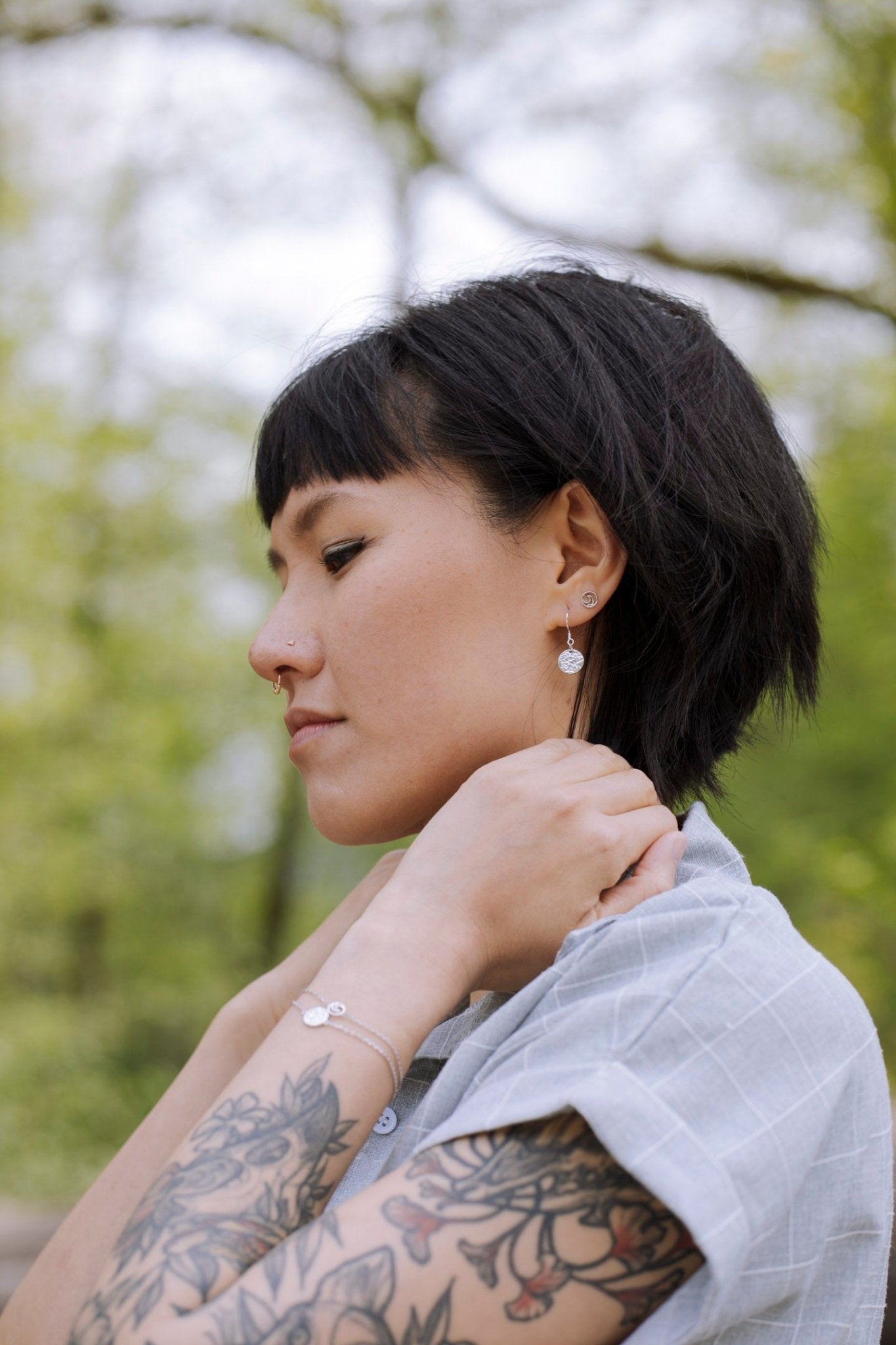 model wearing sterling silver Sol textured circle drop earrings with tree background