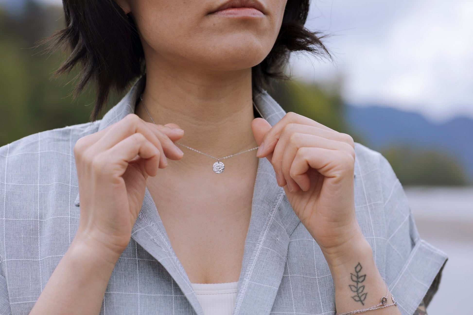 model wearing and holding sterling silver Sol Sun Inspired Small Circle Necklace with nature blur background
