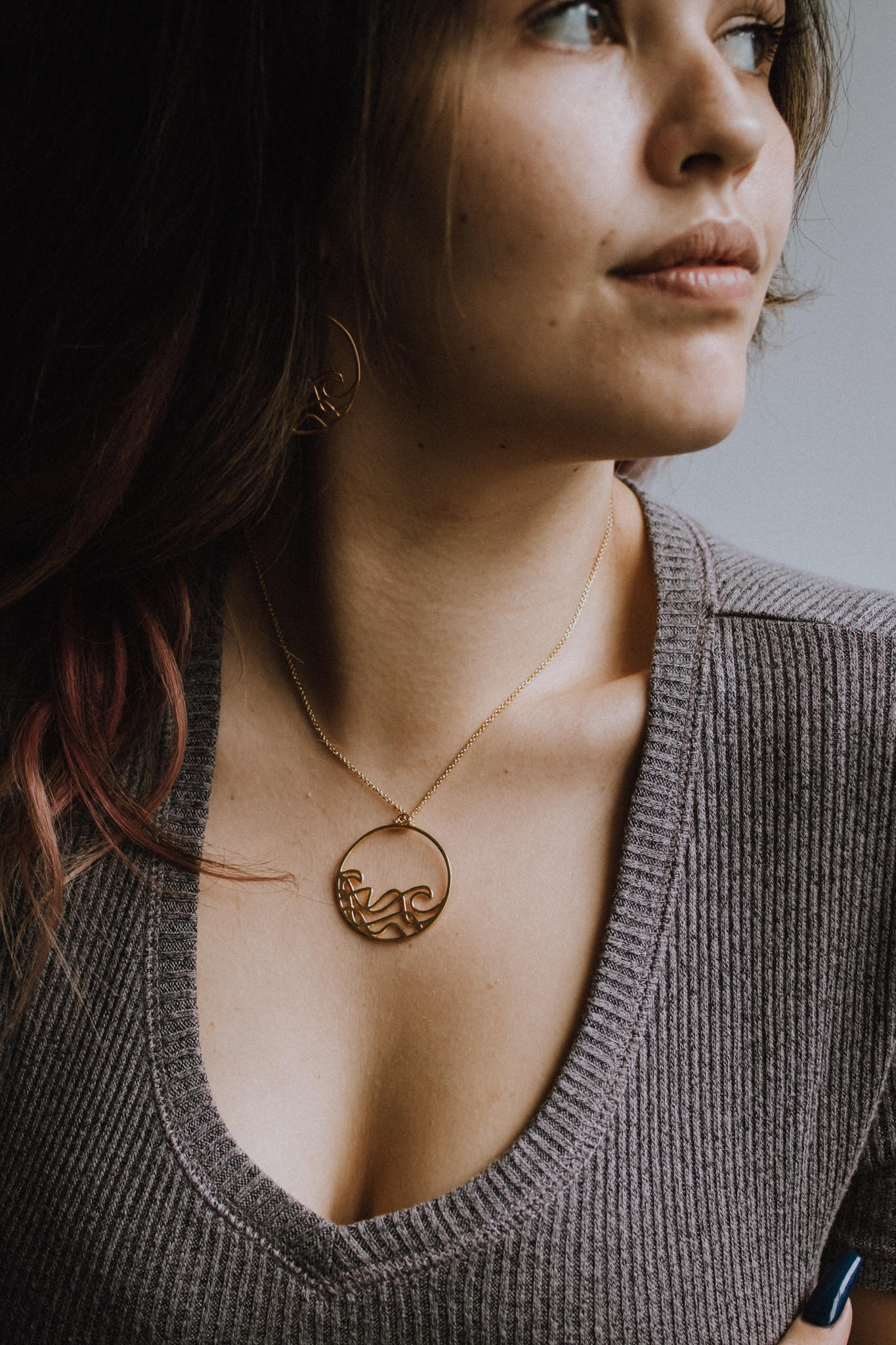 model wearing 18k plated yellow gold round beach wave necklace. surf wave pendant on chain necklace.