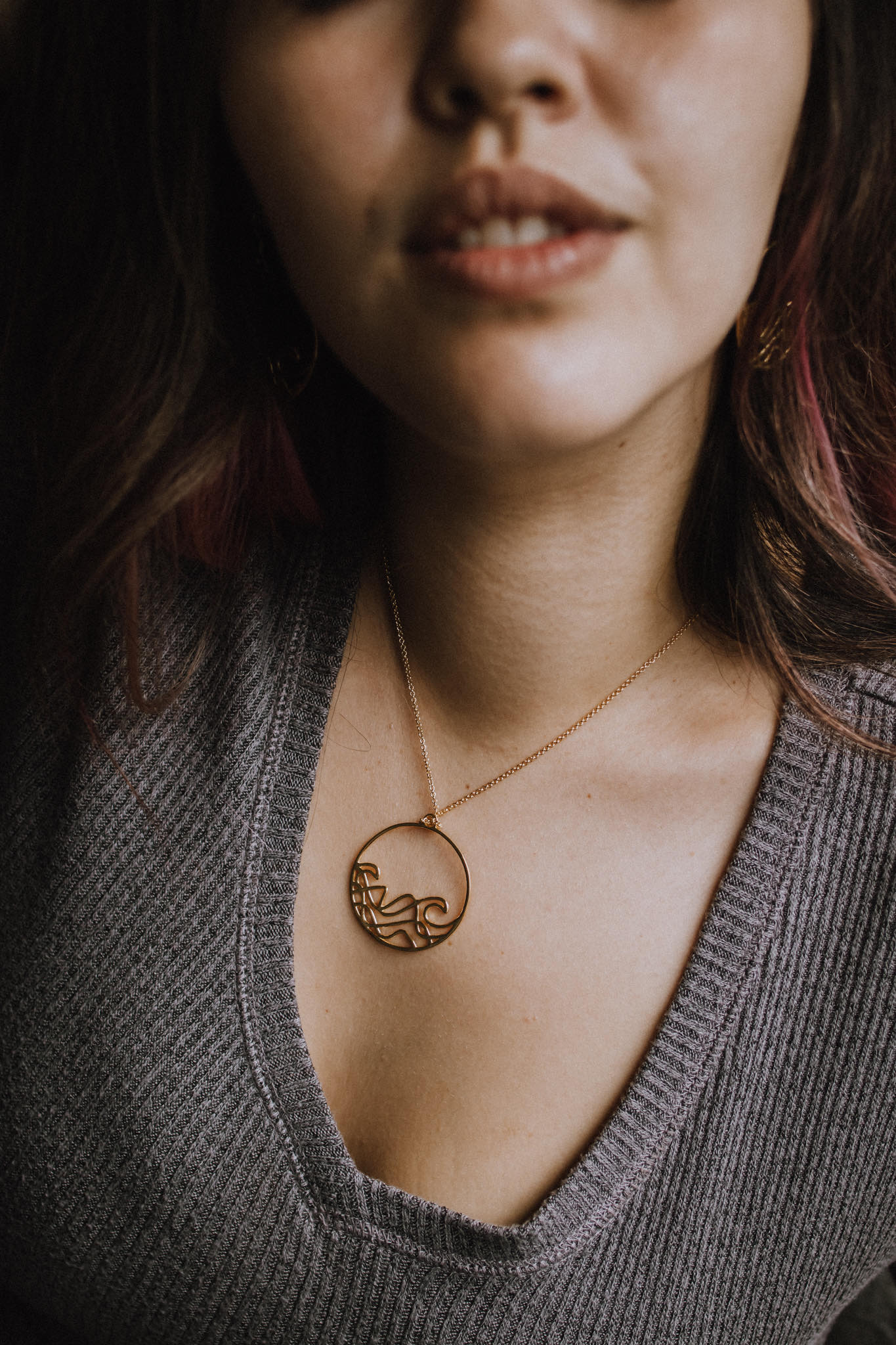 model close up wearing 18k plated yellow gold Sombrio beach  round wave necklace. surf wave pendant on chain necklace.