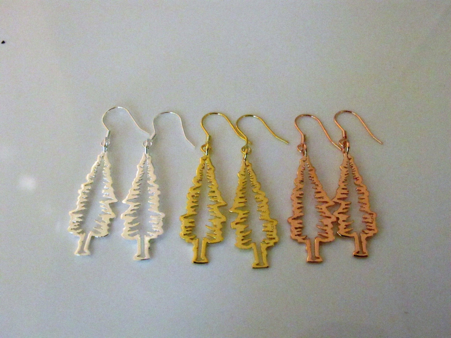 3 pairs of sterling silver fir tree dangle earrings with various gold and rhodium plating. outline of evergreen tree
