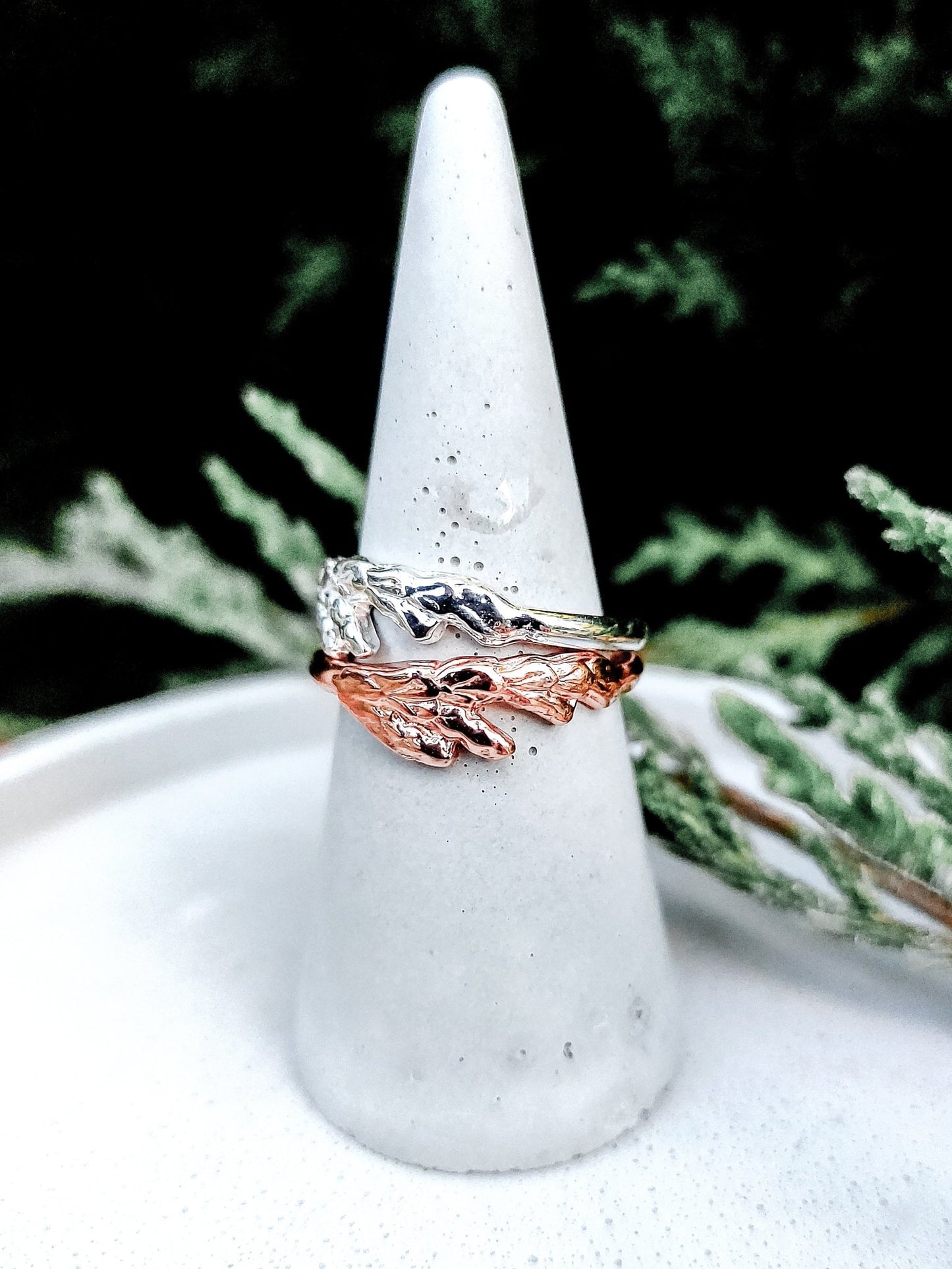 silver and 18k plated rose gold cedar leaf thuja rings shown on ring holder with cedar tree background