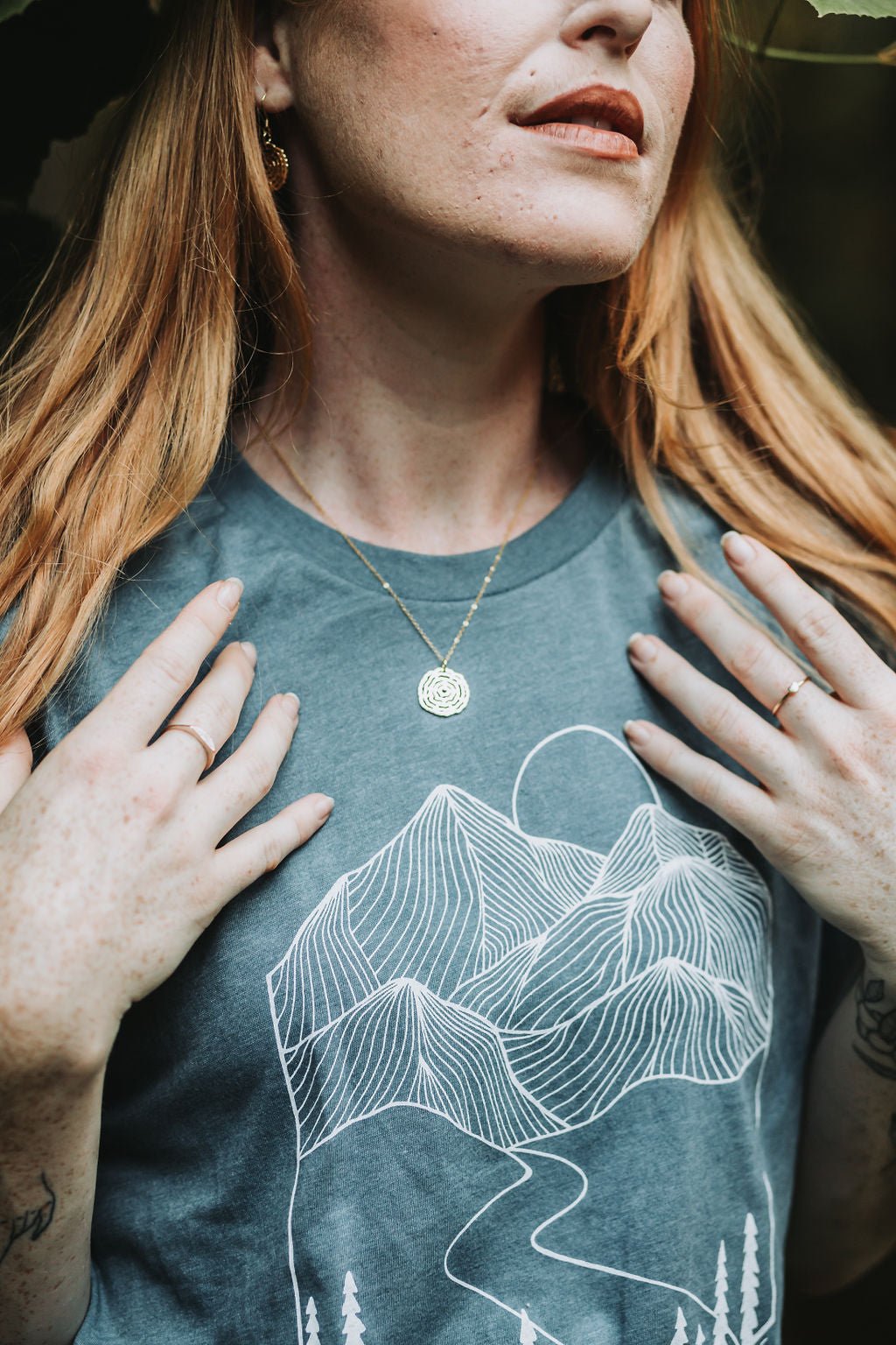 model wearing turquoise shirt and gold vita necklace with both hands shown on her chest framing the necklace